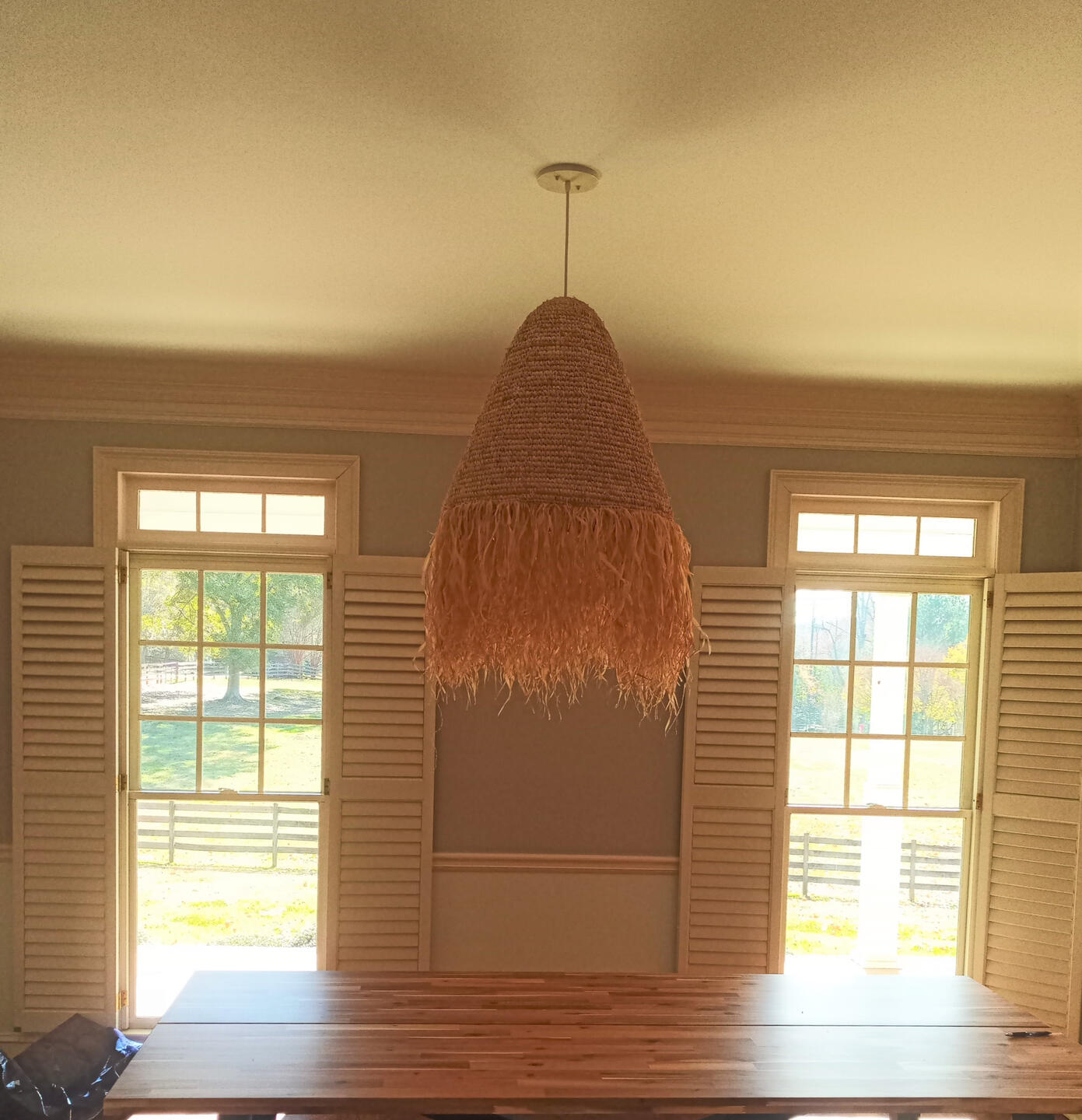 Handy Dandy Atlanta — handwoven rattan pendant lamp with raffia fringe hung from a dining-room ceiling between two french doors